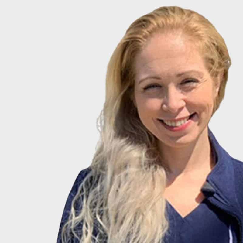 A smiling woman with long blonde hair wearing a navy blue veterinarian shirt, set against a plain white background.